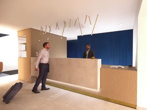 A reception area with a wooden reception desk, a blue wall, and a ceiling with hanging light fixtures. - Hotel Les 3 Clés (Gembloux)