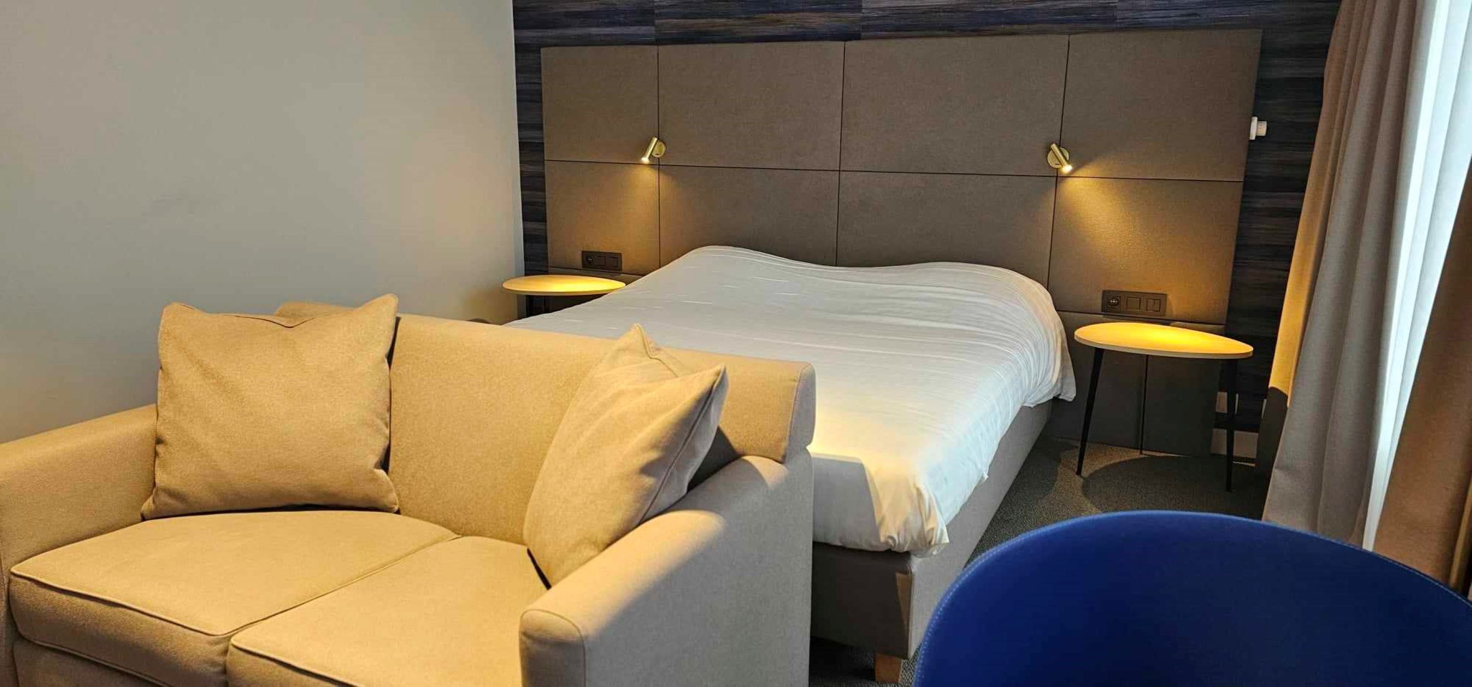 A hotel room with a bed, a sofa, two bedside tables, and a chair.