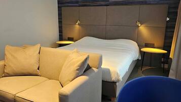 A hotel room with a bed, a sofa, two bedside tables, and a chair.
