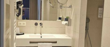 Un baño moderno con lavamanos, espejo y ducha.