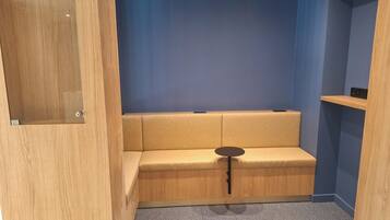 A small, enclosed room with a wooden door, a beige sofa, a small round table, and a blue wall.