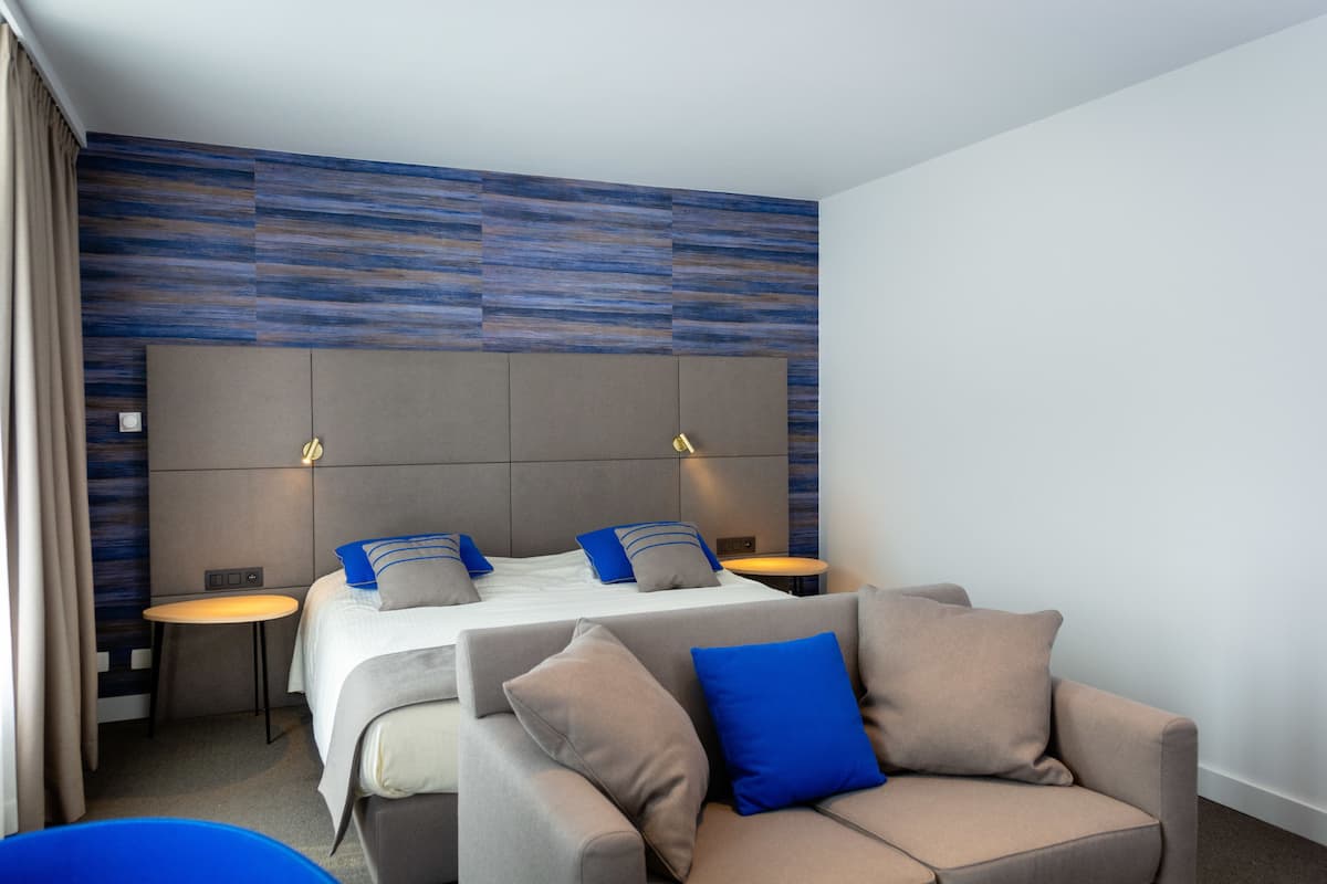 A modern hotel room with a large bed, two bedside tables, a sofa, and a small table.