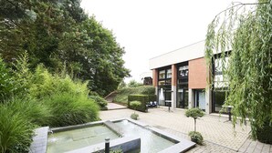 A courtyard with a rectangular water feature, a brick building, and surrounding greenery. - Hotel Les 3 Clés (Gembloux)