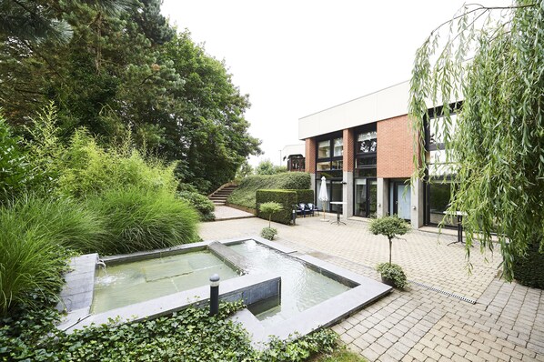 A courtyard with a rectangular water feature, a brick building, and surrounding greenery. - Hotel Les 3 Clés (Gembloux)