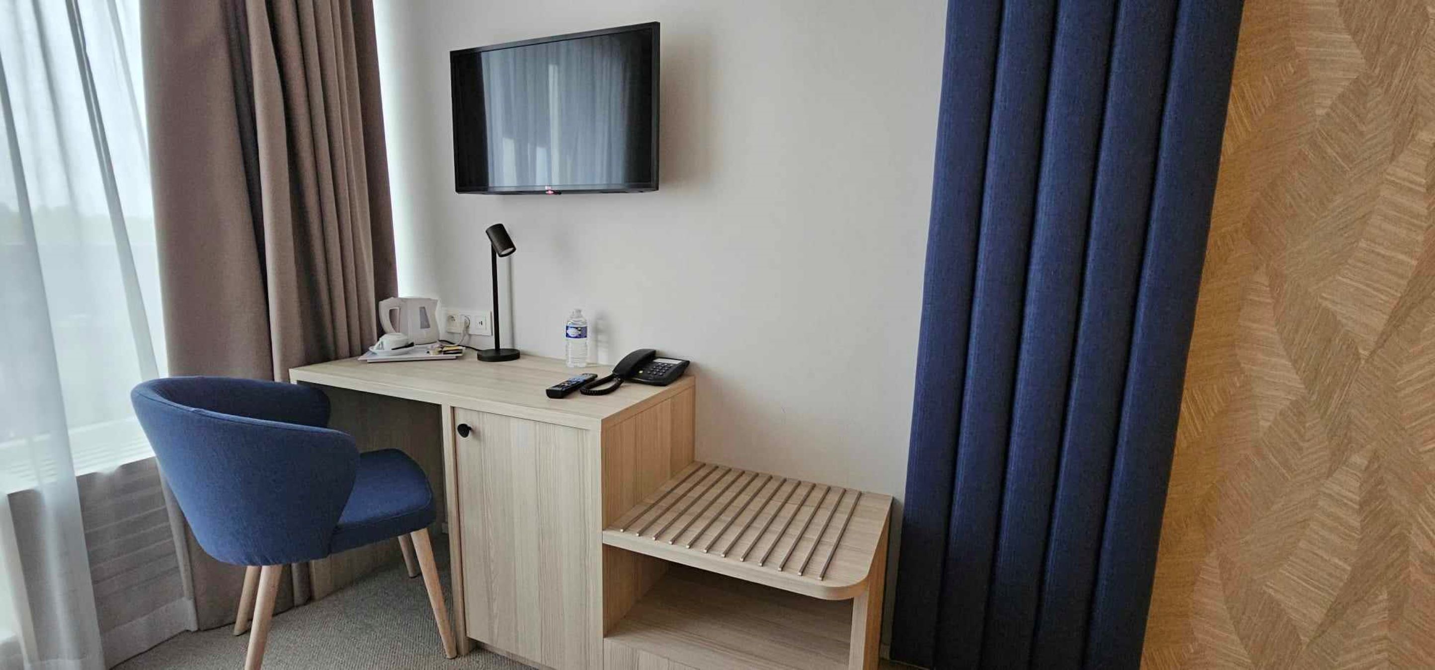 Ein Hotelzimmer mit Schreibtisch, Stuhl, Fernseher und einem kleinen Regal.