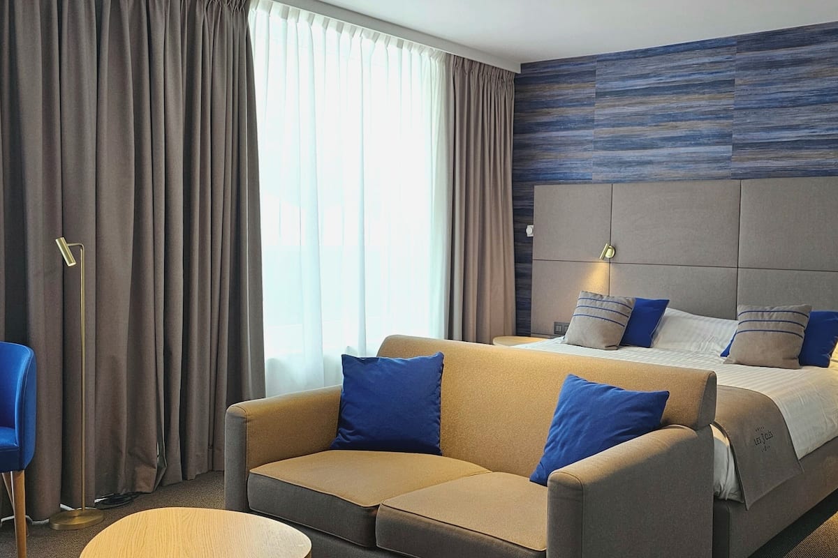 A hotel room with a large bed, a sofa, a small table, and a chair.