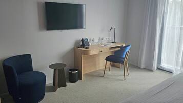 A hotel room with a bed, a desk with a chair, a television, and a window with curtains.
