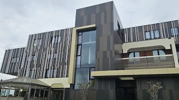 A modern building with a mix of vertical and horizontal paneling, large windows, and a covered outdoor seating area.