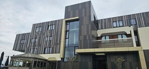 A modern building with a mix of vertical and horizontal paneling, large windows, and a covered outdoor seating area. - Hotel Les 3 Clés (Gembloux)