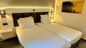 Habitación de hotel con dos camas individuales, cabeceras, lámparas de noche y un cuadro colgado en la pared.