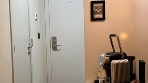 Una habitación de hotel con una cama, un escritorio con cafetera y un cartel de bienvenida enmarcado.