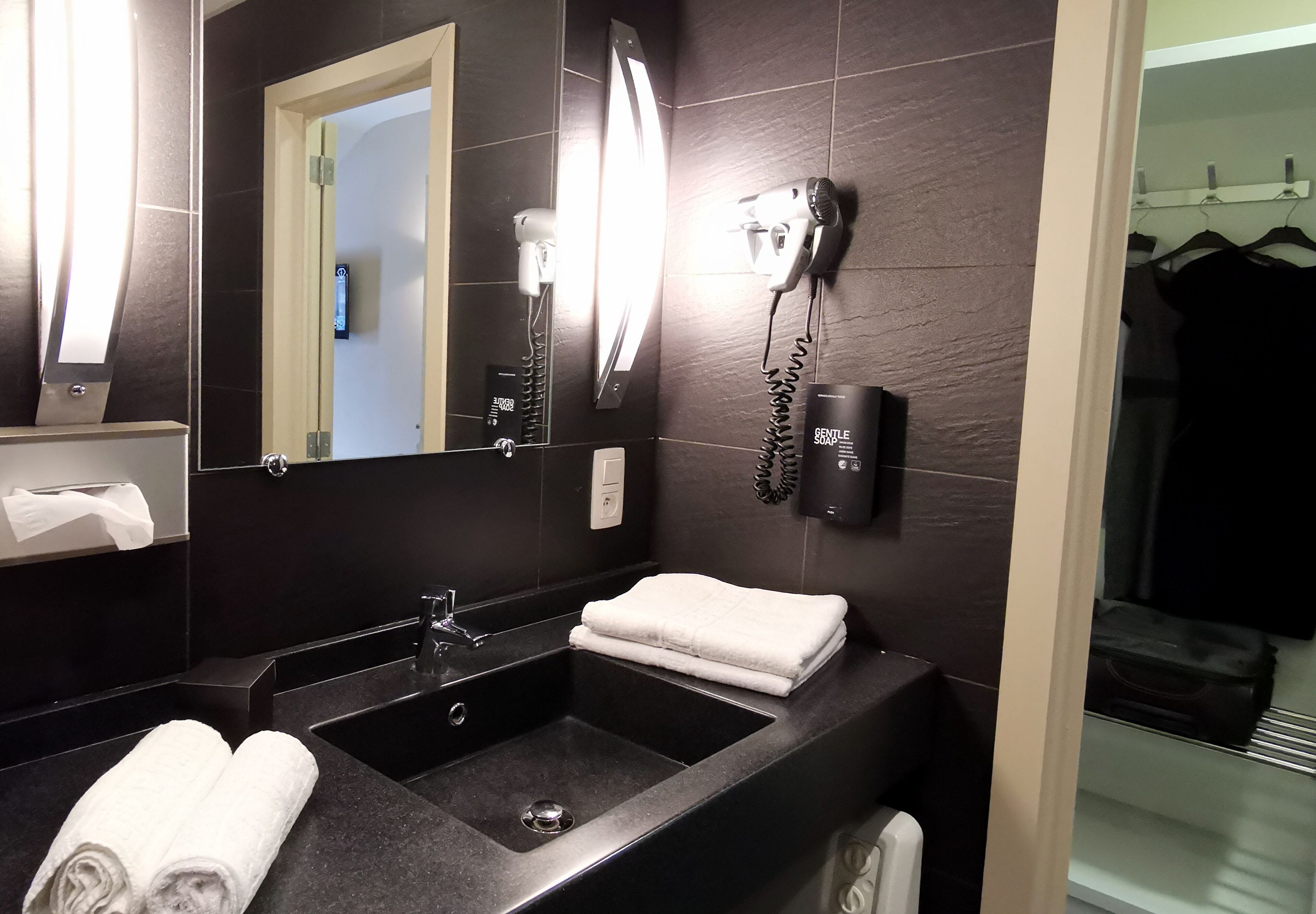 Un baño moderno con un lavabo negro, un espejo, un secador de pelo y un perchero para toallas.