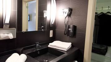 Un baño moderno con un lavabo negro, un espejo, un secador de pelo y un perchero para toallas.