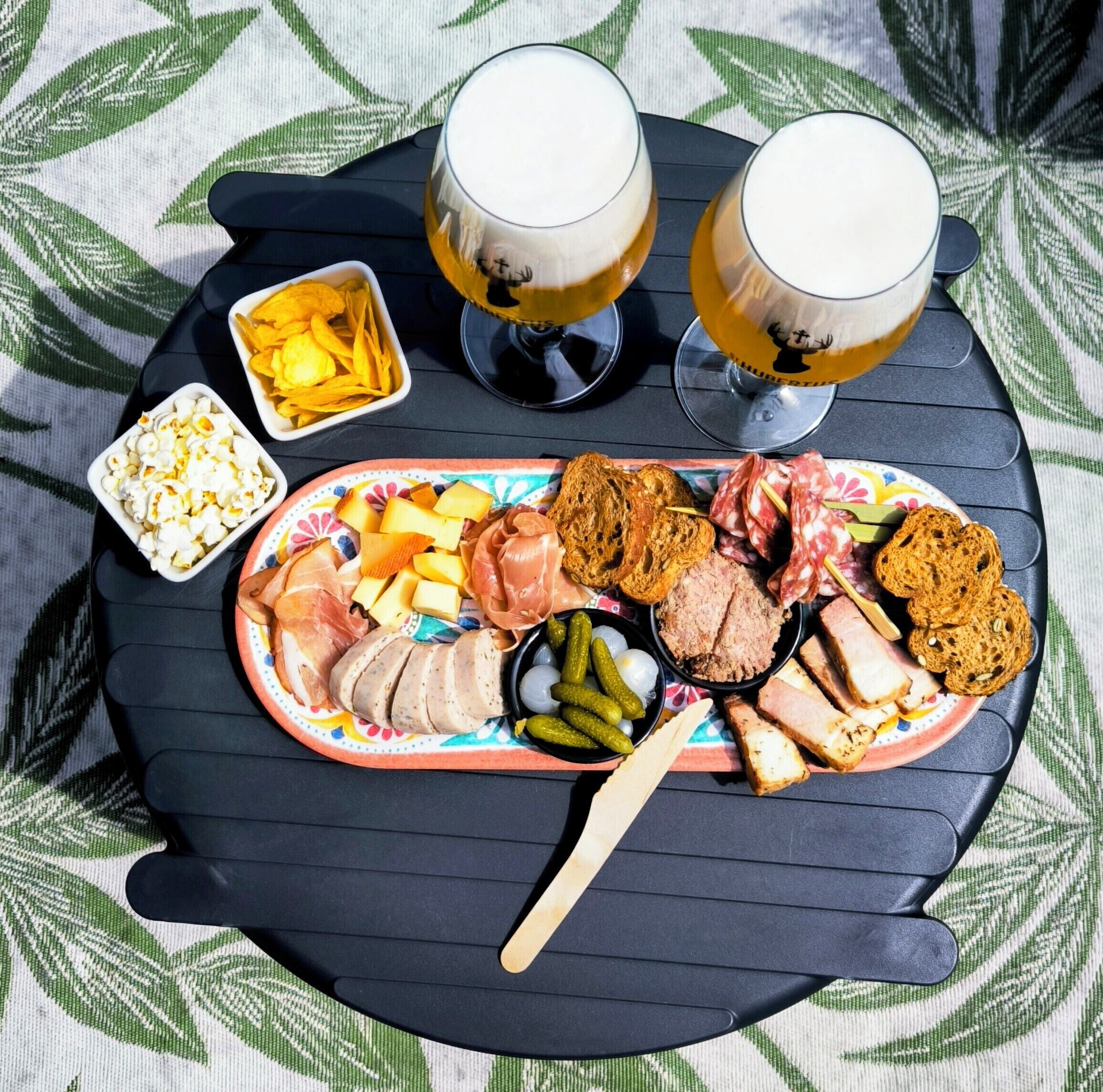 Une table dressée avec une assiette de nourriture, deux verres de bière et un bol de chips.