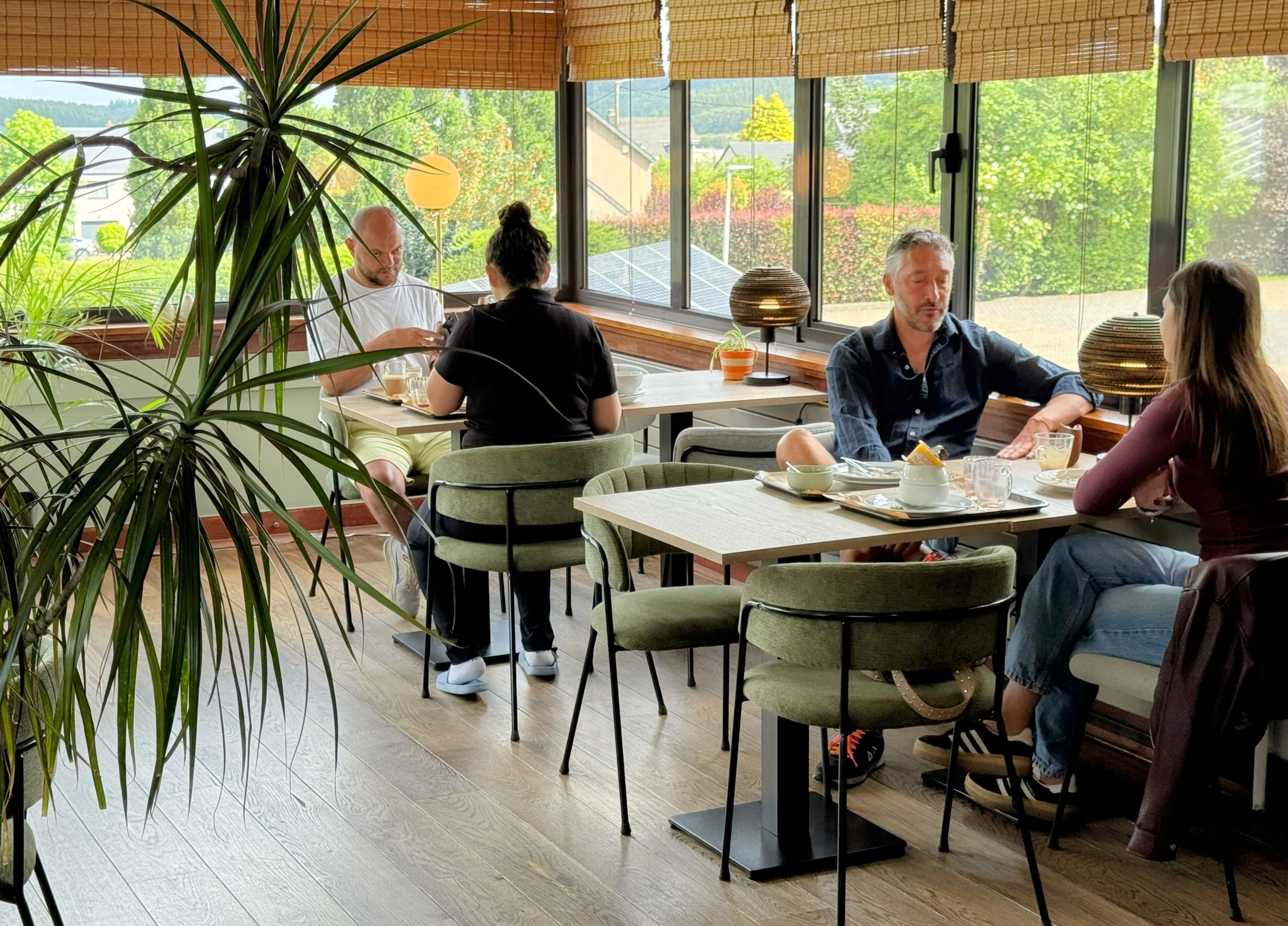 Un ristorante con posti a sedere interni, ampie finestre e piante in vaso.