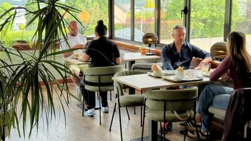 Un ristorante con posti a sedere interni, ampie finestre e piante in vaso.