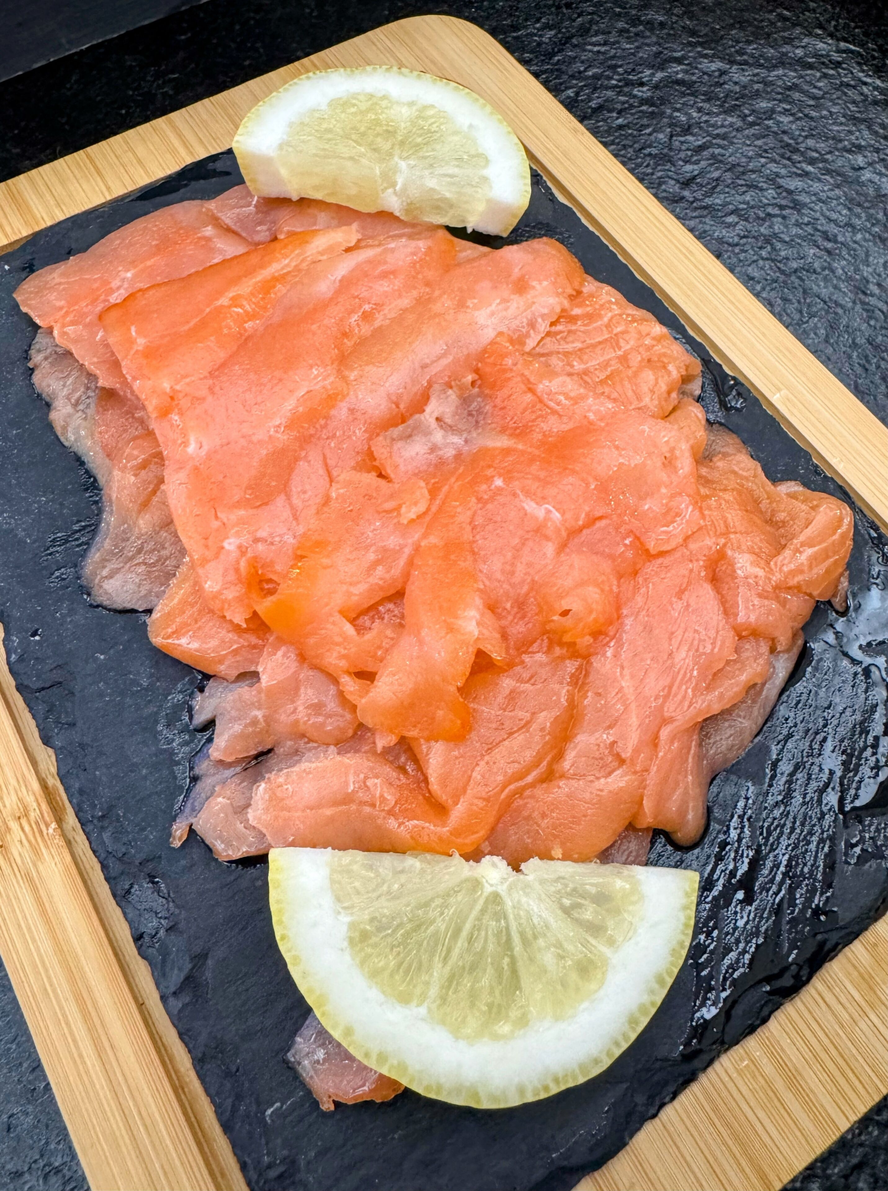Een plak rauwe zalm op een zwarte leisteenplaat met houten randen.