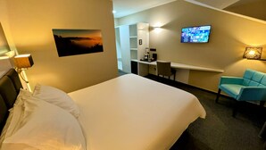 Habitación de hotel con cama, escritorio, silla, televisor y lámpara de pared.