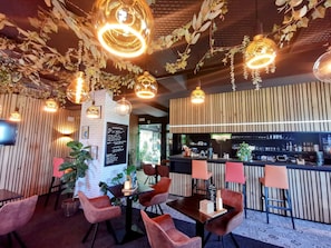 A restaurant with wooden panel walls, hanging pendant lights, and a bar area with stools. - Hotel L' Amandier (Libramont-Chevigny)