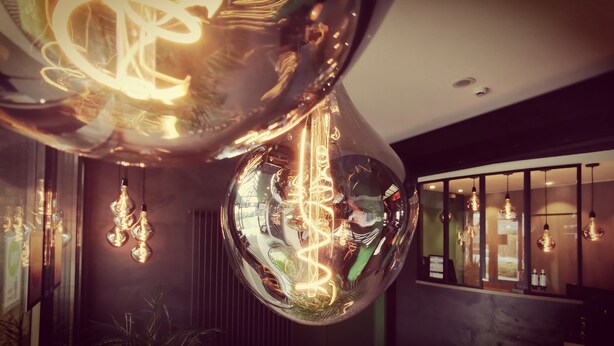 Un interior moderno con espejos esféricos que reflejan luminarias, una zona de recepción con mostrador y una pared de tonos oscuros.