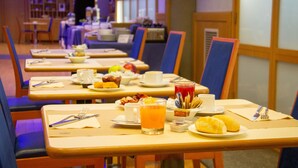 Una escena de desayuno con mesas preparadas para comer, incluyendo platos de comida, tazas y un vaso de zumo de naranja.