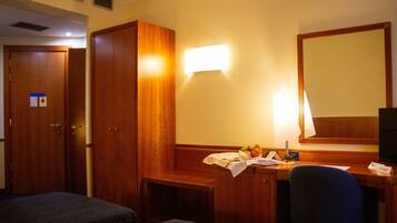 Una habitación de hotel con dos camas individuales, un armario de madera, un escritorio con lámpara y un espejo.