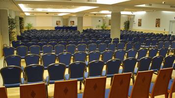 A conference room with rows of blue chairs and a stage area.