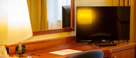 A wooden desk with a television, a lamp, and a remote control.
