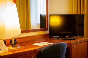 A wooden desk with a television, a lamp, and a remote control.