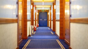 Un pasillo de hotel con alfombra azul, paneles de madera y una puerta azul al final.