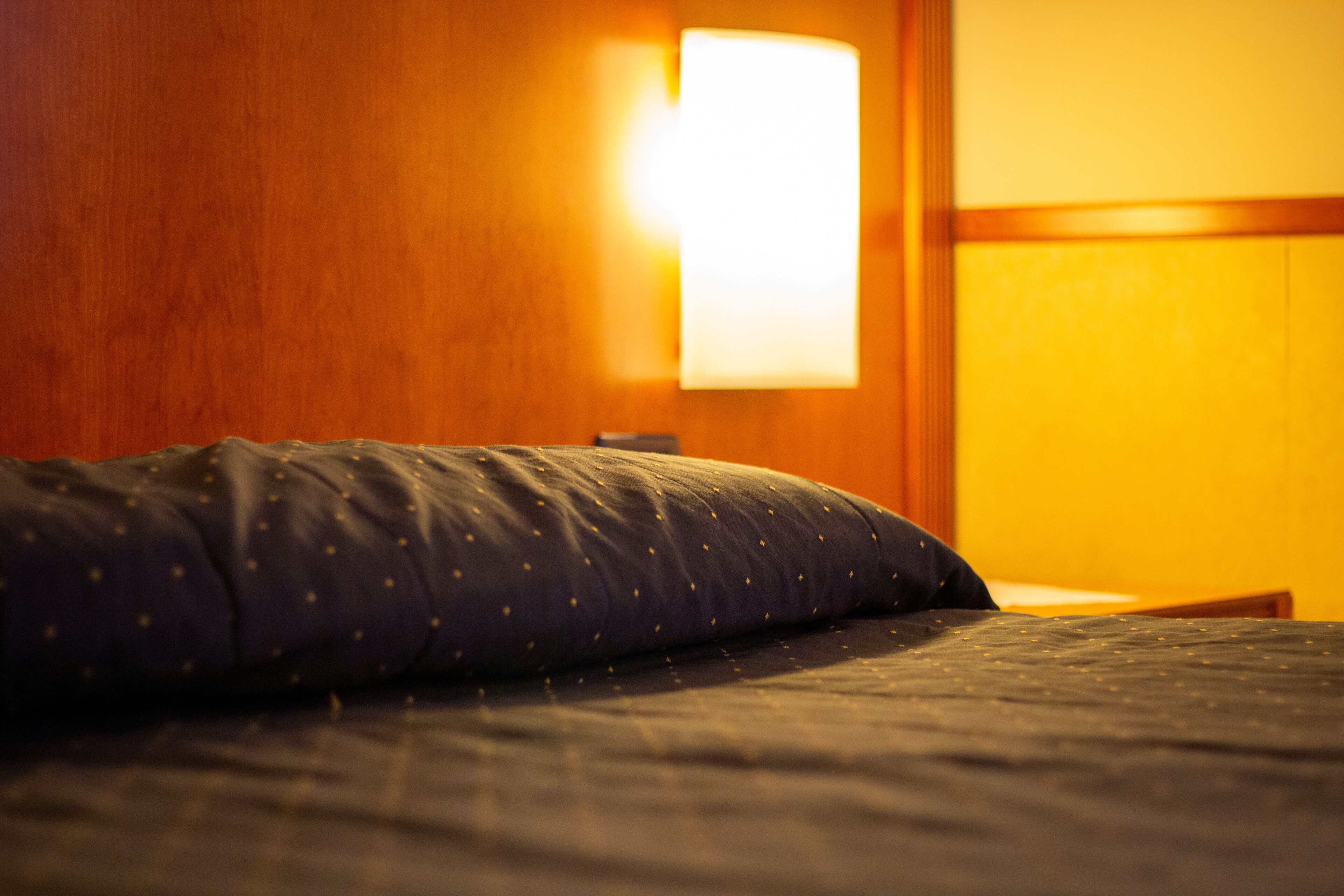 A bed with a dark blue quilt and a wooden headboard.