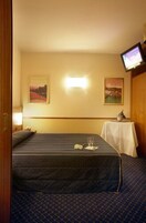 A hotel room with a single bed, a small table with a lamp, and a television on the wall.