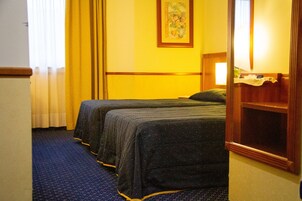 A hotel room with two beds, a large mirror, a painting on the wall, and a window with curtains.