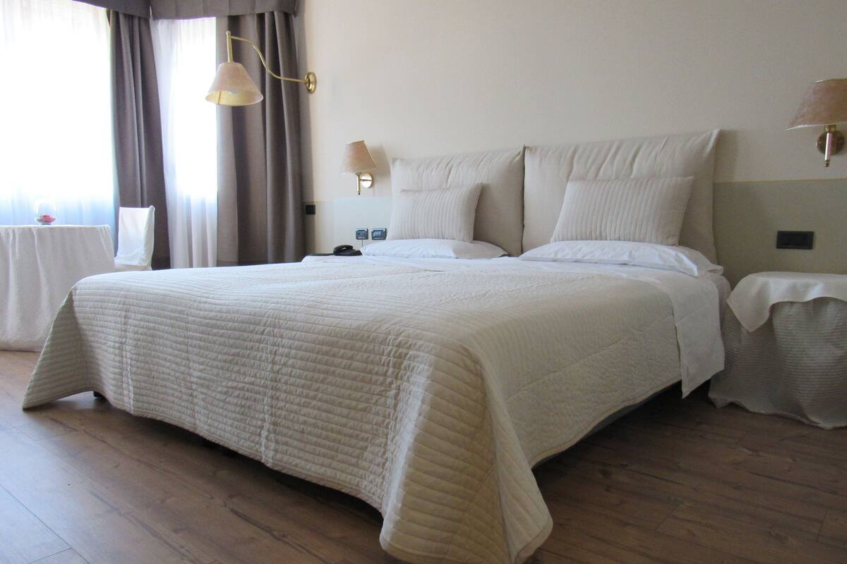 A large bed with a quilted bedspread, a bedside table with a lamp, and a nightstand with a lamp.