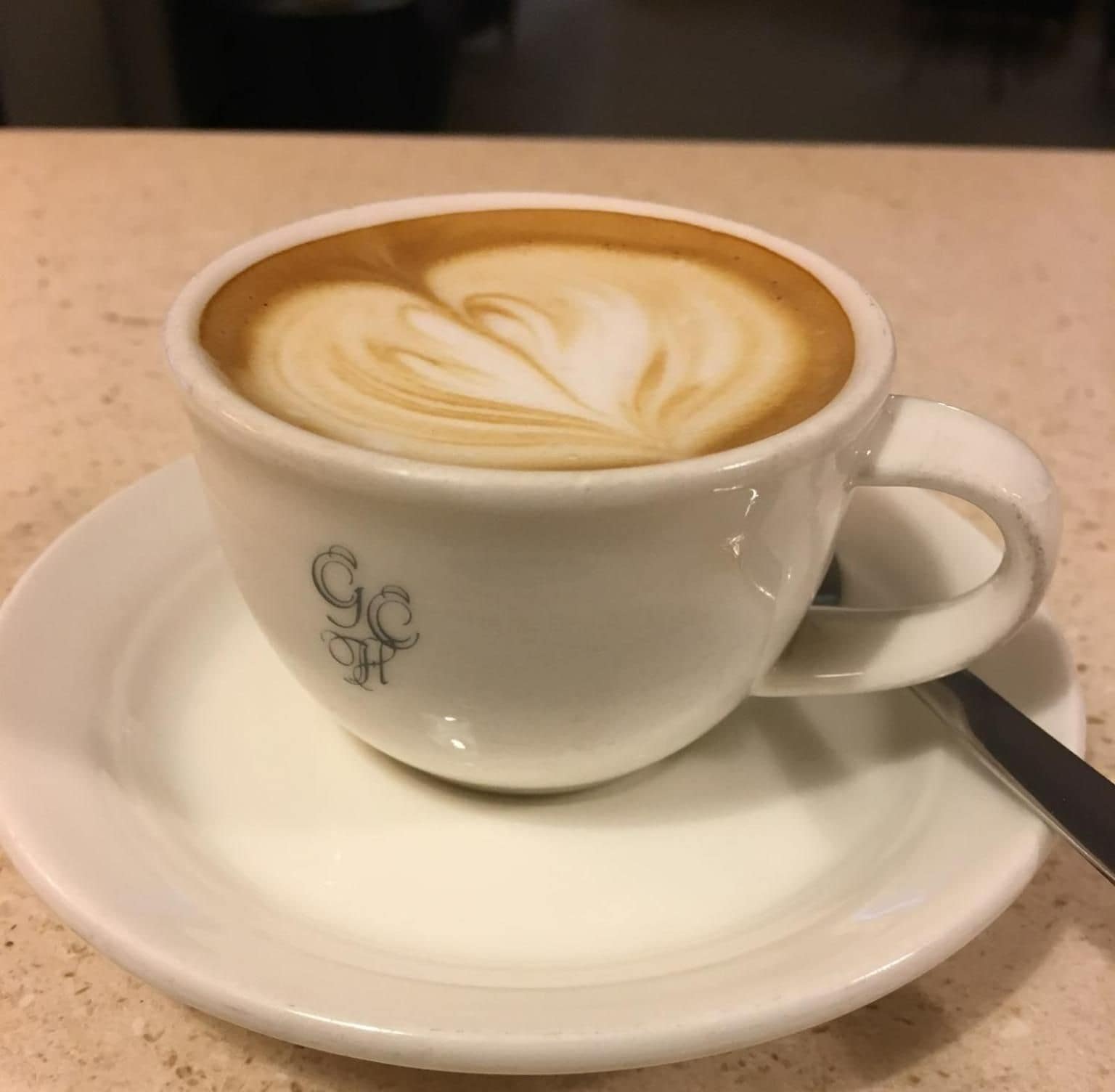En kopp kaffe med vackra mönster i mjölkskummet, serverad på ett litet fat.