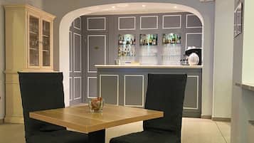 A dining area with a table and chairs, a bar area with shelves of bottles, and a cabinet with glassware.