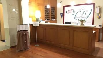 A hotel reception area with a wooden reception desk, a framed sign above it, and a wall-mounted information board.