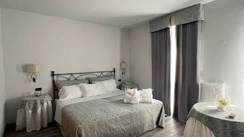 Habitación de hotel ordenada con una cama grande, mesitas de noche, una pequeña mesa con un florero y una ventana con cortinas.
