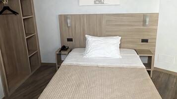 A hotel room with a large bed, a wooden wardrobe, a bedside table with a phone, and a wall-mounted light.