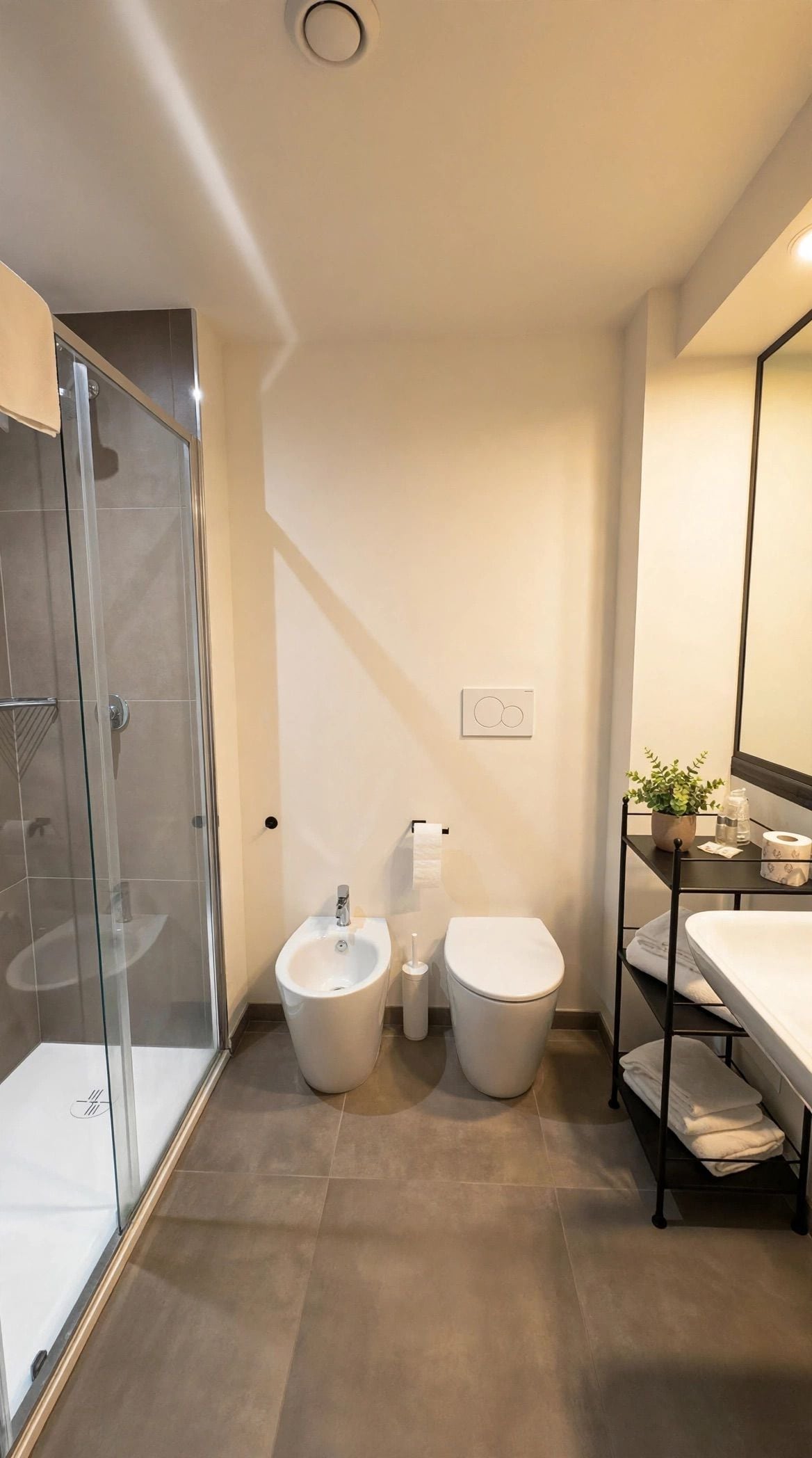 Un bagno moderno con box doccia in vetro, un bidet, un water e uno scaffale con asciugamani.