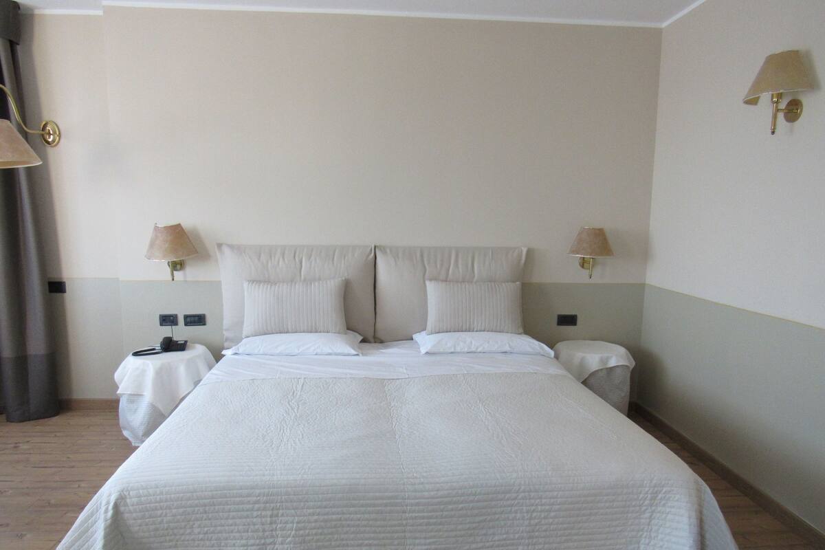 A neatly made bed with a white duvet, two bedside lamps, and a nightstand with a phone.