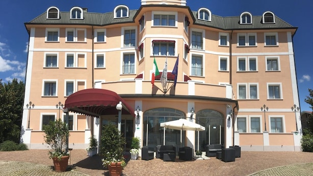Een meerhoog hotel met een centrale ingang, een terras en vlaggen.