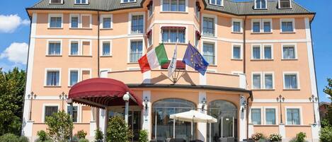 A multi-story hotel with a central entrance, outdoor seating, and flags.