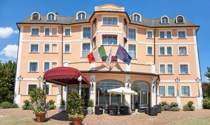 A multi-story hotel with a central entrance, outdoor seating, and flags.
