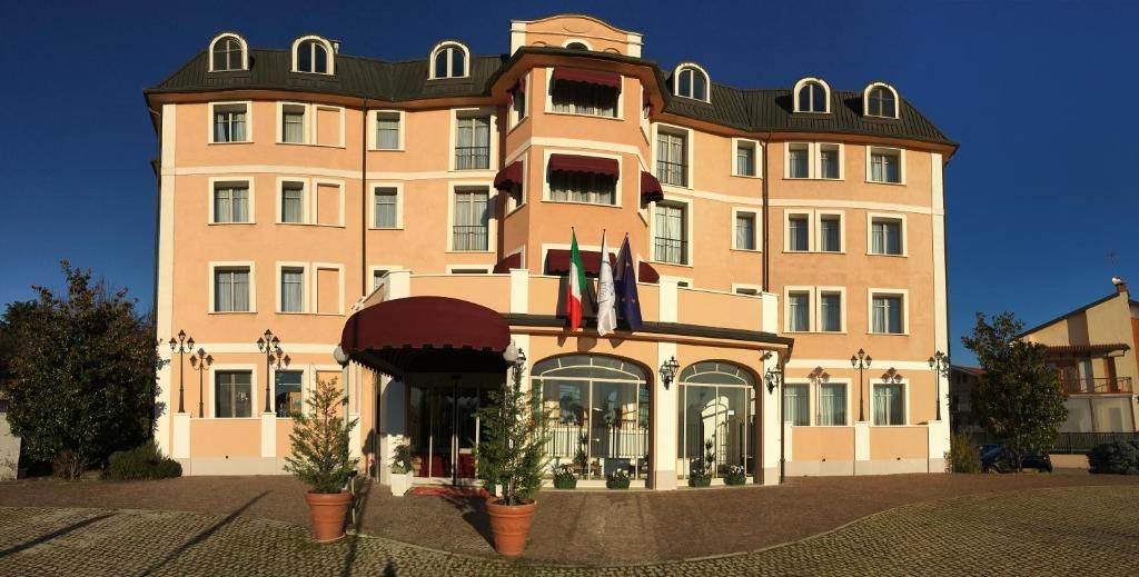 Un hotel de varios pisos con una entrada central, banderas y un área cubierta con plantas en macetas.