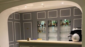 Una zona de bar con mostrador, estantes llenos de botellas de licor y vasos.