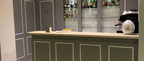 A bar area with a counter, shelves of liquor bottles, and glasses.