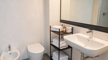 A modern bathroom with a white sink, a bidet, a toilet, and a towel rack with folded towels.