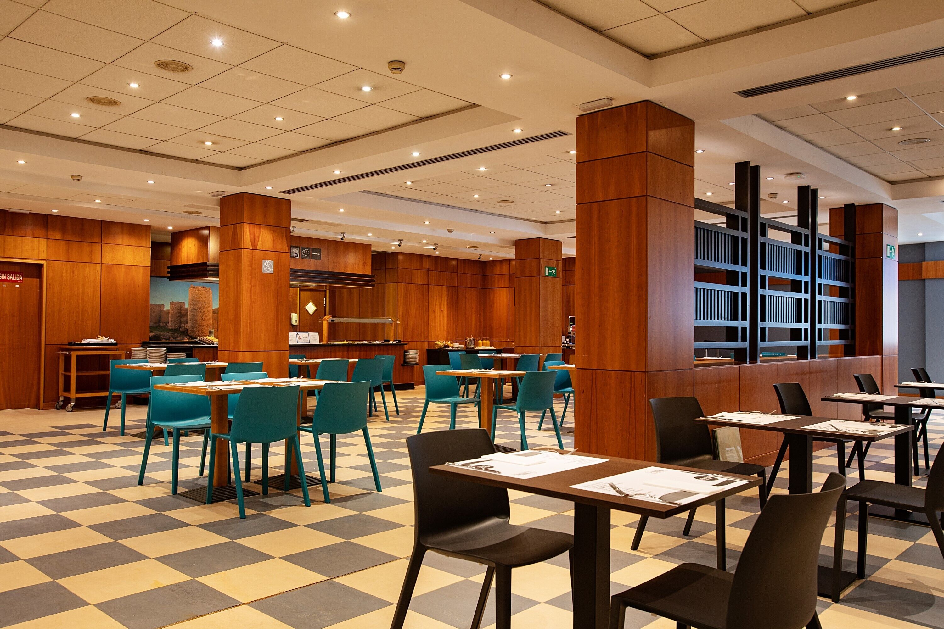 Un vestíbulo de hotel con suelo a cuadros, paneles de madera y sillas color turquesa.