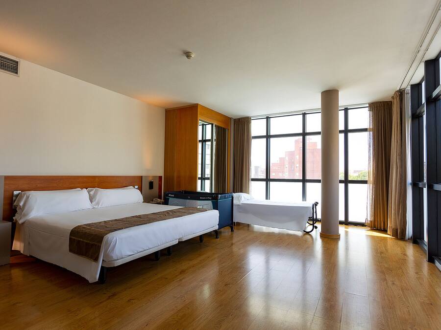 A hotel room with a large bed, a desk, a chair, a wardrobe, and a window with curtains.